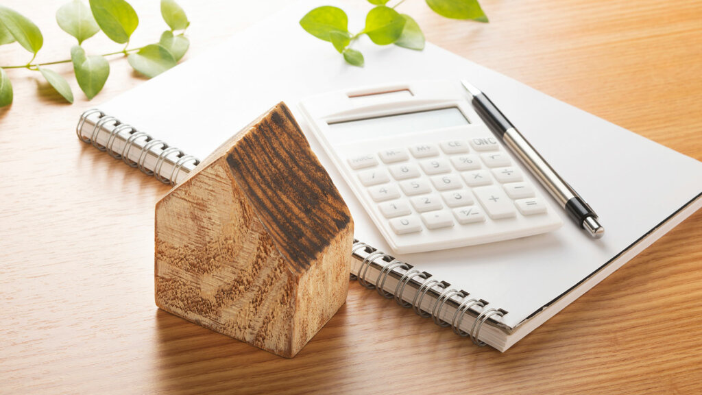 Wooden house next to notepad and calculator