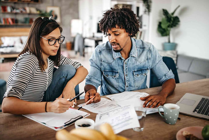 Saving hacks couple assessing finances in their home sitting at the dining room table