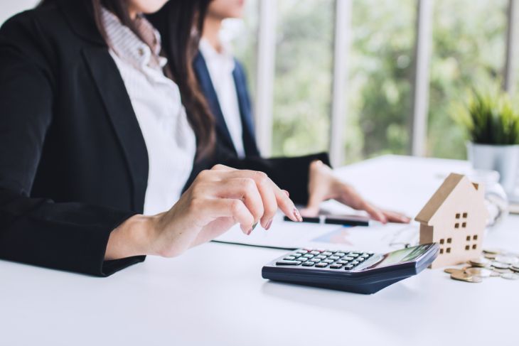 Two female conveyancers doing admin with wooden house ornament and calculator on the table